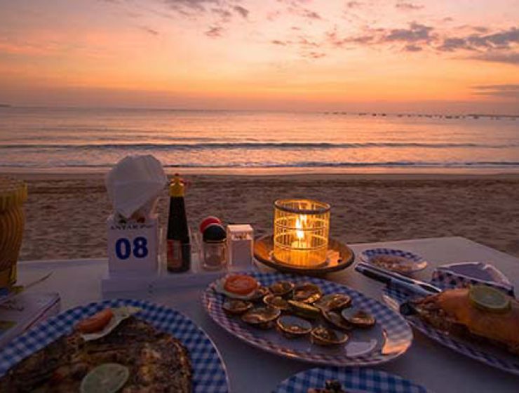 A wide-angle evening view of a curated coastal dining experience in Jimbaran, showcasing a seamless integration of landscape and service as part of an Apex Tour.