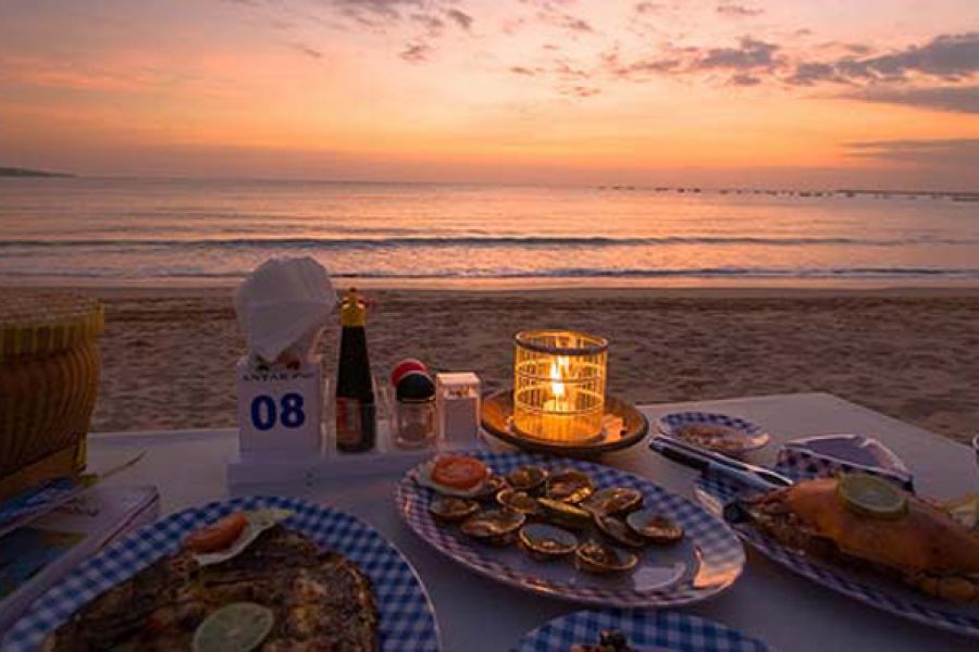 A wide-angle evening view of a curated coastal dining experience in Jimbaran, showcasing a seamless integration of landscape and service as part of an Apex Tour.
